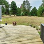 Holzterrasse mit Sitzgruppen und Blick auf Grünfläche mit Spielgeräten und Bäumen.