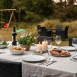 Garten-Tisch mit Speisen, Kerzen und Wein. Hintergrund: Schaukel und Gras.