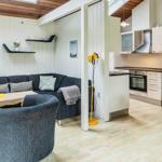 Wohnbereich mit Sofa, Esstisch und Küche. Holzfußboden und weiße Wände.