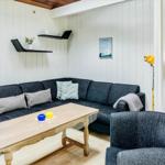 Wohnzimmer mit Sofa, Tisch und Sessel. Küche und Eingangsbereich sichtbar.