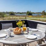 Rundtisch mit Frühstück auf Terrasse mit Blick auf Wasser und Wiesen.
