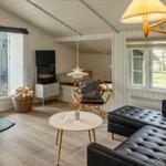 Wohnzimmer mit Kamin, Sofa und Fernseher. Holzdielen und große Fenster.