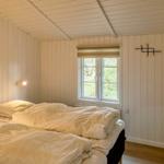 Schlafzimmer mit Doppelbett, Fenster und Holzwandverkleidung.