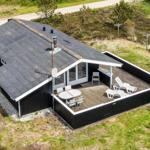 Schwarzes Haus mit Terrasse, Tisch, Stühlen und Liegestühlen im Grünen.
