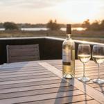 Auf der Terrasse steht ein Tisch mit Wein und Gläsern. Im Hintergrund ist eine Landschaft bei Sonnenuntergang zu sehen.