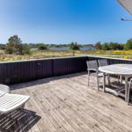 Terrasse mit Tisch, Stühlen und Liegestuhl. Blick auf Grünland und Wasser.