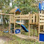 Holzspielplatz mit Schaukel, Rutsche und Piratenschiff im Wald.