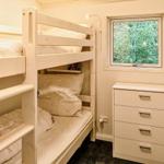 Zimmer mit Doppelstockbett, Schrank und Fenster mit Blick auf Bäume.
