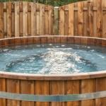 Holzwhirlpool mit Metallbändern im Garten, umgeben von Holzzäunen.