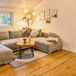 Wohnzimmer mit Ecksofa, Holzboden und Tisch. Durchgang zu Schlafzimmer.