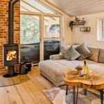 Wohnzimmer mit Kamin, Sofa und Holztisch. Große Fenster und Tür zur Terrasse.