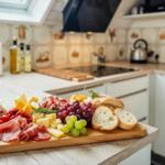 Küche mit Holzbrett, Käse, Wurst, Obst und Brot.