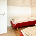 Zwei Betten mit weißen Bettwäsche in einem Raum mit Holzboden und weißen Wänden.