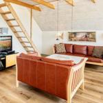 Wohnzimmer mit Sofa, Sessel und TV. Holzdecke und Treppenhaus sichtbar.