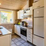 Küche mit Arbeitsplatte, Spüle, Kühlschrank und Herd. Holzwände und Fenster mit Blick.