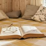 Ein Buch mit Brille liegt auf einem gemusterten Boden vor Fenster und Kissen.