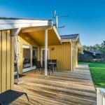 Gelbes Ferienhaus mit Holzterrasse und Garten. Tisch und Stühle sind draußen.
