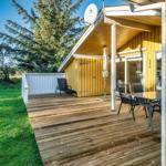 Holzterrasse mit Tisch, Stühlen und Sonnenschirm neben gelbem Haus.