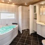 Badezimmer mit Whirlpool, Waschbecken und Toilette. Holzdecke und Fliesenboden.