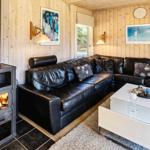Wohnzimmer mit Holzwand, schwarzer Ledercouch, Kamin und Glas-Tisch.