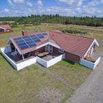 Rotes Dach mit Solarpaneelen, weiße Umzäunung, Grillplatz und Sitzgelegenheiten im Garten.