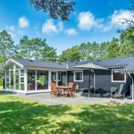 Moderne Ferienhaus mit Terrasse, Garten und Spielplatz unter Bäumen.