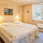 Schlafzimmer mit Holzwand, Bett und Fenster mit Blick auf Außenbereich.