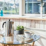 Glas-Tisch mit Kaffeekanne und Tassen vor Fenster mit Holzverkleidung.