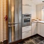 Küche mit Edelstahl-Kühlschrank und Backofen, weißer Arbeitsfläche und Fensterblick auf Grünfläche.