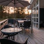 Terrasse mit Tisch, Stühlen und Sonnenschirm. Blick auf Wald bei Sonnenuntergang.