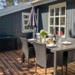 Terrasse mit Tisch, Stühlen und Sonnenschirm vor grauem Haus