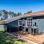 Haus mit Terrasse, Tisch, Stühlen und Sonnenschirm. Hintergrund: Wald und klarer Himmel.