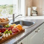 Küche mit Arbeitsplatte, Spüle und Kühlschrank. Auf dem Tisch steht ein Käse- und Obsttablett.