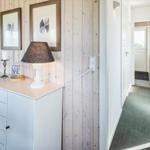 Flur mit weißen Türen und Holzwand. Schrank mit Lampe und Bildern.