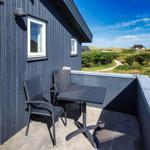Terrasse mit Tisch und Stühlen vor einem dunkelblauen Haus mit Blick auf grüne Hügel.