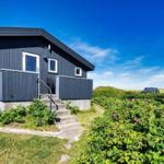 Moderne Strandhütte mit Terrasse und Garten. Blick auf Dünen und klaren Himmel.