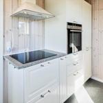 Küche mit weißen Schränken, Induktionskochfeld und Backofen. Nebenraum mit Toilette und Wohnzimmer.