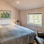 Schlafzimmer mit Bett, Ledersessel und Holzwandverkleidung. Fenster mit Blick auf Bäume.