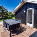 Terrasse mit Tisch und Stühlen vor einem Haus mit dunklem Holzverkleidung.