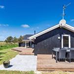 Schwarzes Holzhaus mit Terrasse und Garten. Satellitenschüssel und Außentisch sichtbar.