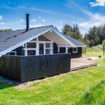 Moderne Holzhütte mit Terrasse und Garten. Umgeben von Bäumen unter blauem Himmel.