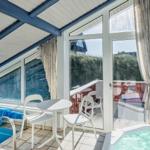 Innenbereich mit Pool, Whirlpool und Sitzgelegenheit. Große Fenster bieten Blick auf Außengelände.