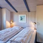 Zimmer mit zwei Betten, Holzwand und Deckenbalken, Wandbild und Nachttischlampen.