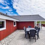 Rotes Holzhaus mit Terrasse und Gartenmöbeln unter blauem Himmel.