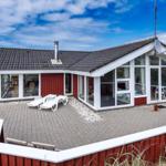 Rotes Ferienhaus mit großem Terrassenbereich und Sicht auf Dünen.