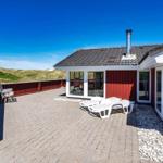Rotes Ferienhaus mit Terrasse und Liegen. Blick auf Dünen unter blauem Himmel.