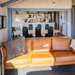 Ein braunes Ledersofa mit Kissen und Decke. Im Hintergrund ist die Küche mit Esstisch und Stühlen sichtbar.