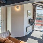 Wohnzimmer mit Sofa, Fernseher und Blick auf Balkon und Pool.