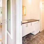 Badezimmer mit Waschmaschine, Toilette und Dusche. Küche und Schlafzimmer sind sichtbar.