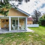 Haus mit überdachter Terrasse und Glasveranda. Weiße Möbel und grüner Garten.